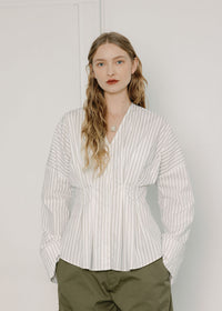 Woman wearing a white striped shirt and green pants against a plain background