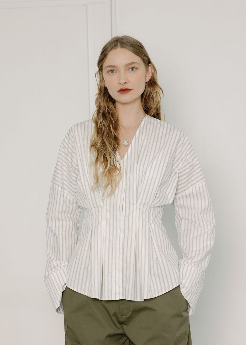 Woman wearing a white striped shirt and green pants against a plain background