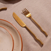Brass fork and knife on a textured beige surface with a ceramic plate.