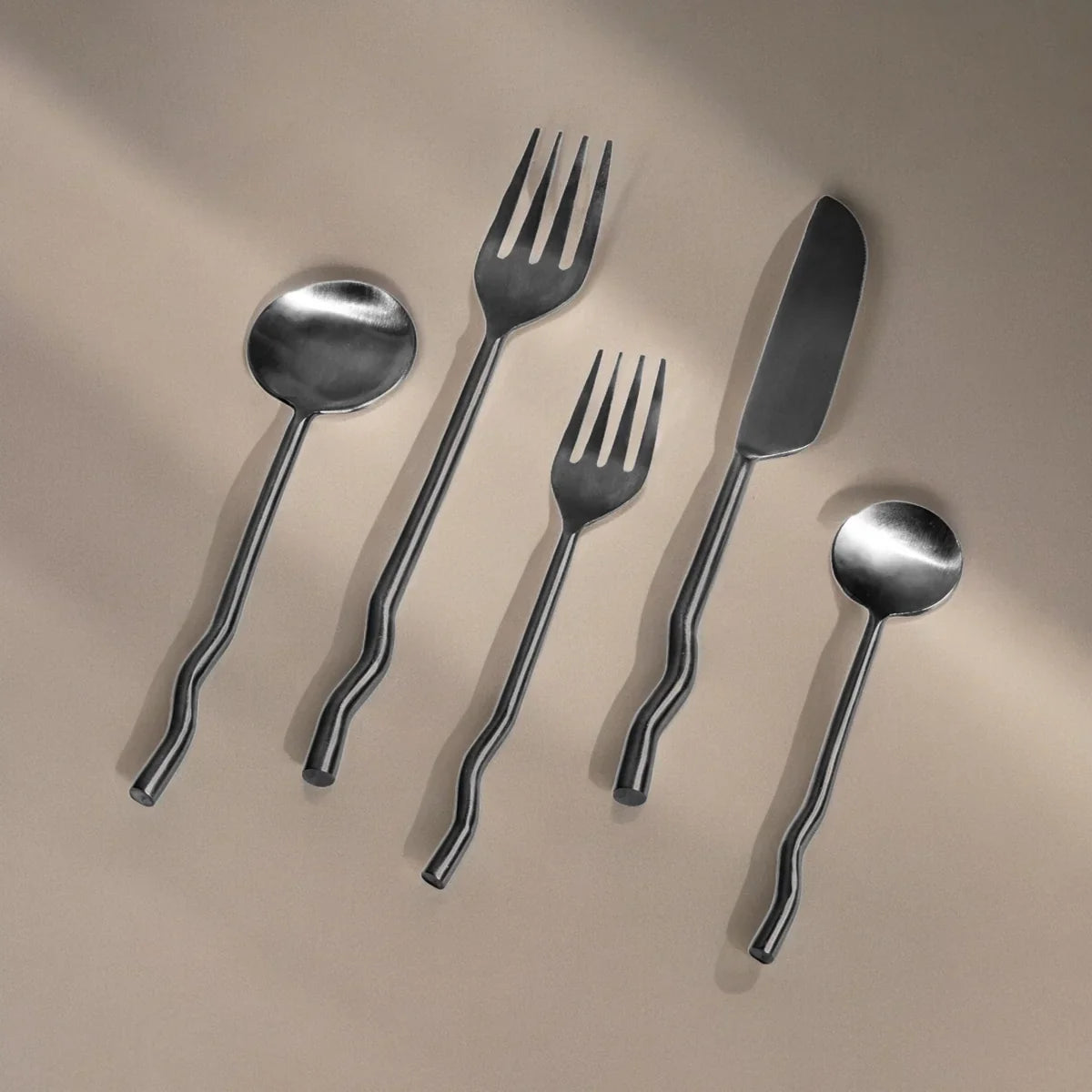 Set of silver cutlery including spoon, fork, and knife on a beige background