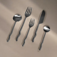 Set of silver cutlery including spoon, fork, and knife on a beige background