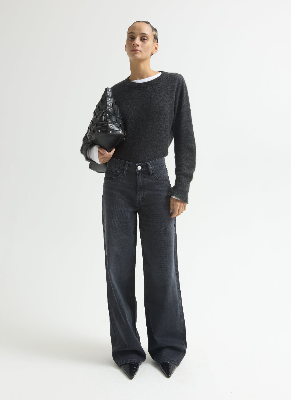 Person wearing a dark gray sweater and jeans holding a black bag on a white background