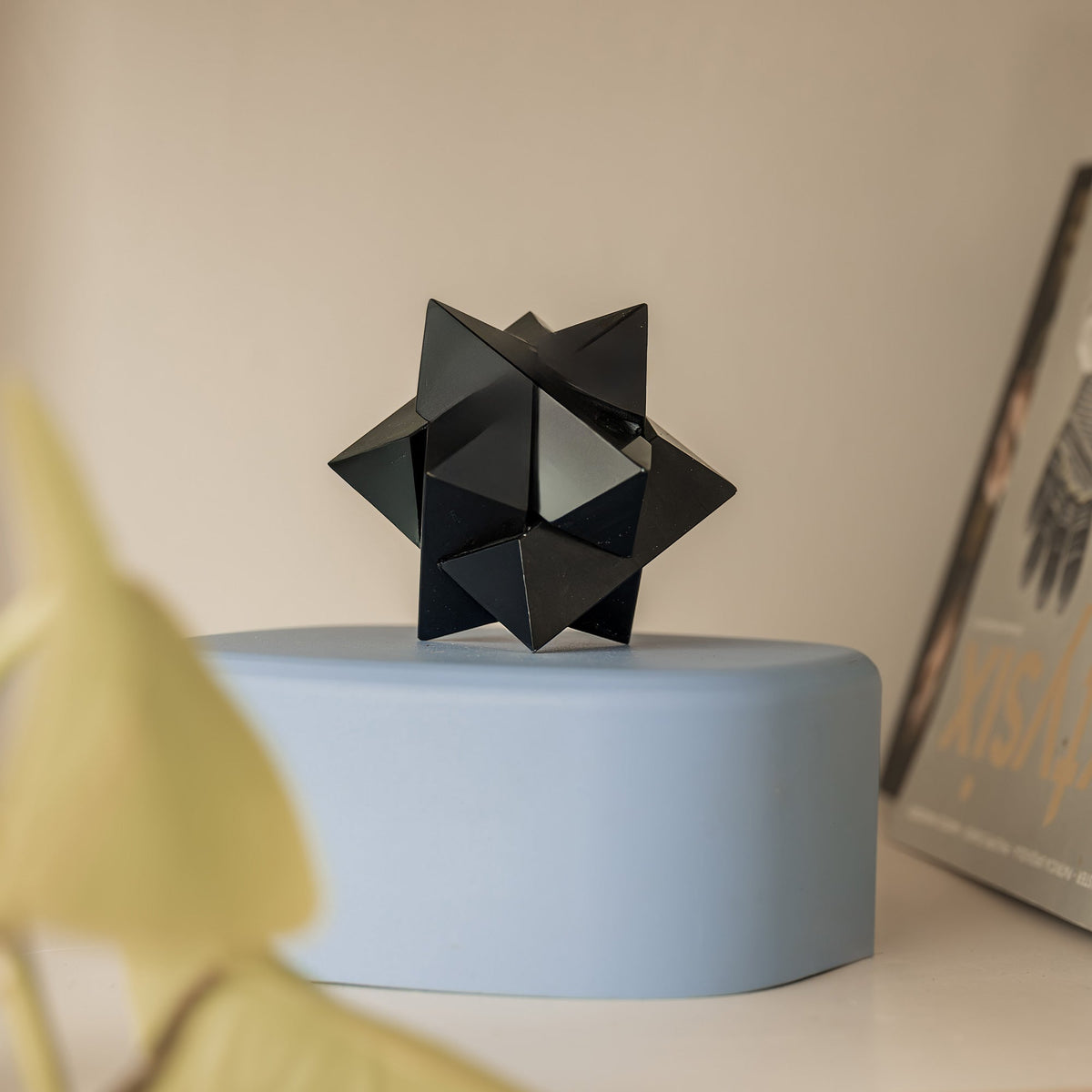 Black geometric sculpture on a blue base against a neutral background