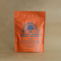 Orange bag of Forest Bathing Bath Soak with blue graphics and text on a Kraft paper background