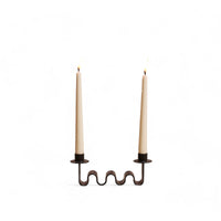 black metal wavy candle holder with two white candles on a white background