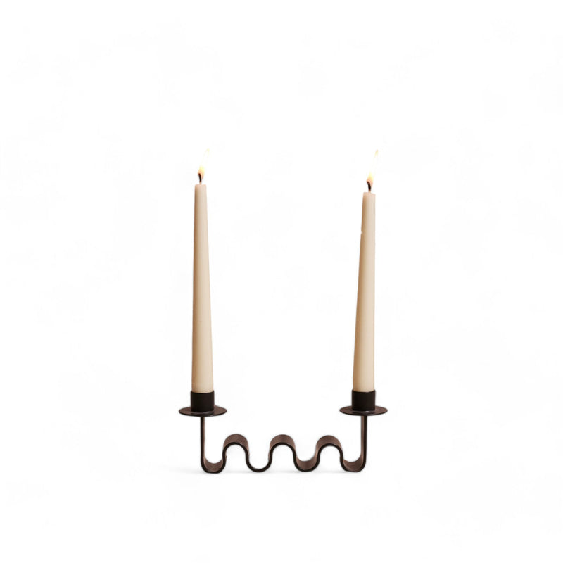 black metal wavy candle holder with two white candles on a white background