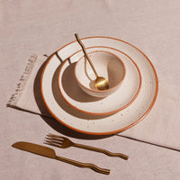 Ceramic plates with gold rim and brass cutlery on a beige surface