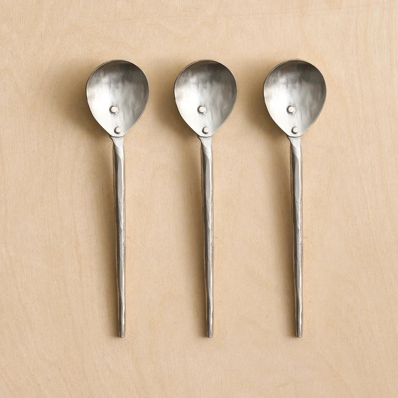Three small pewter spoons on a wooden surface