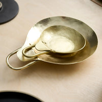 Pair of brass spoon rests stacked on a wooden surface