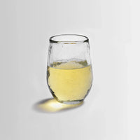Small pebbled drinking glass filled with liquid on a white background