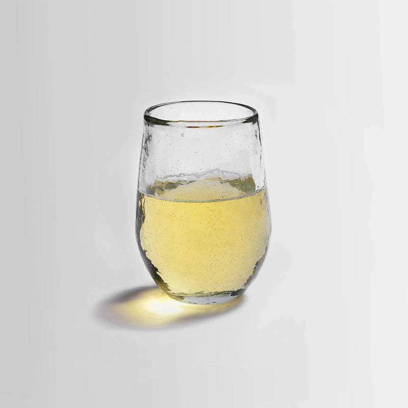 Small pebbled drinking glass filled with liquid on a white background