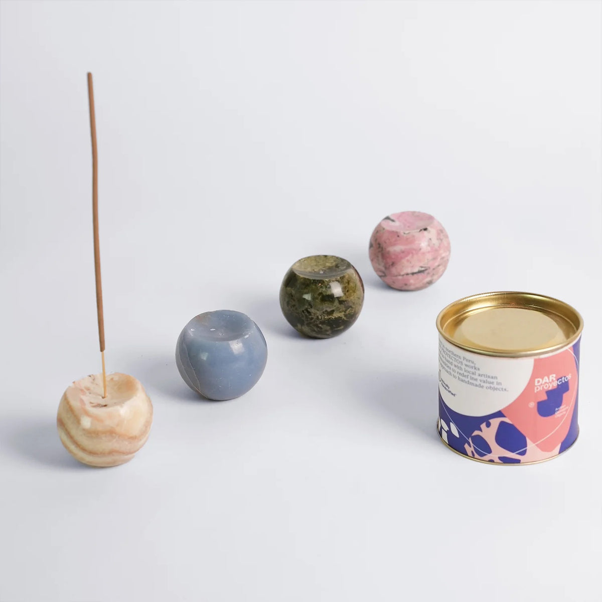 Collection of decorative items including a can, small sphere incense holders, and an incense stick on a light background
