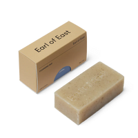 Beige cleansing bar of soap next to an 'Earl of East' branded cardboard box