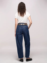 Backside of a person wearing dark blue jeans belted, a white tee, and black loafers in front of a white background