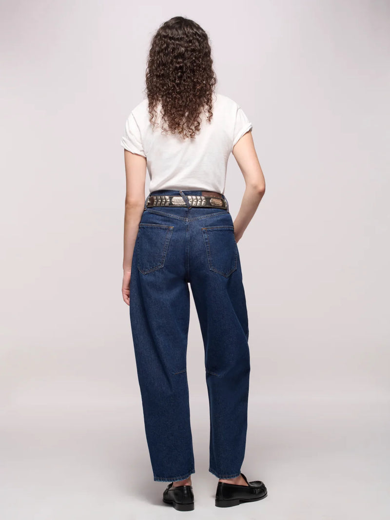 Backside of a person wearing dark blue jeans belted, a white tee, and black loafers in front of a white background