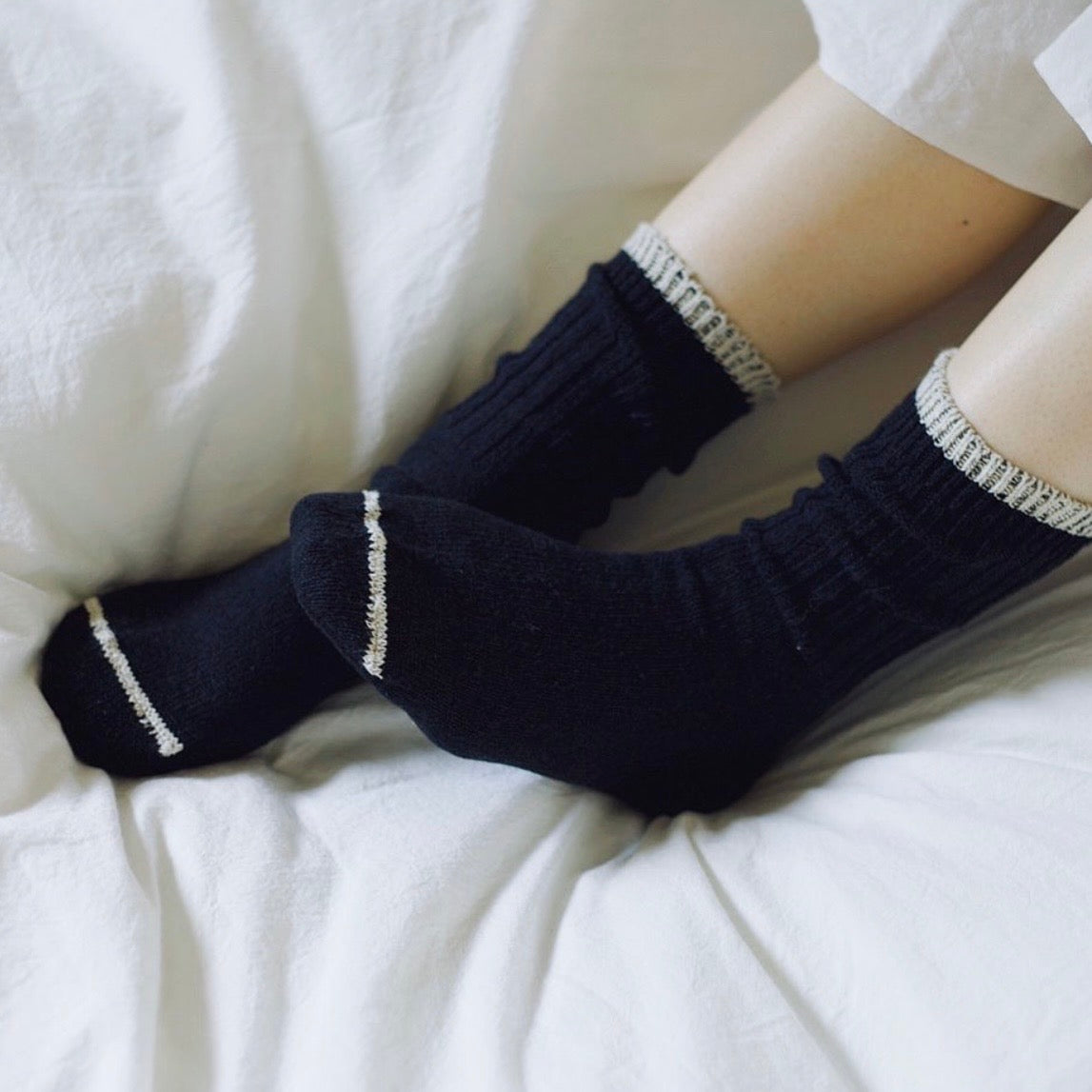 Person's feet wearing black ankle socks with a speckled beige trim and toe stripe on a white fabric cushioned surface