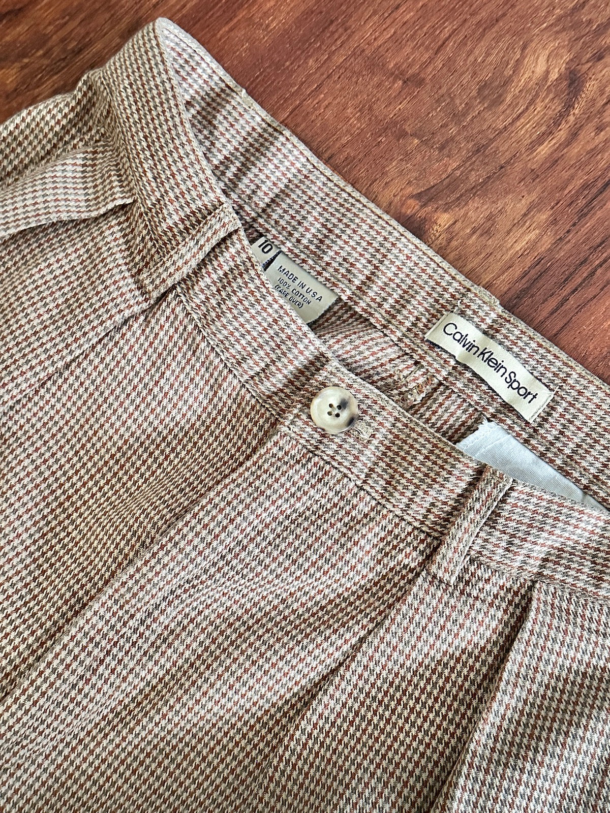 Close-up of brown houndstooth trousers with Calvin Klein Sport label on a wooden surface