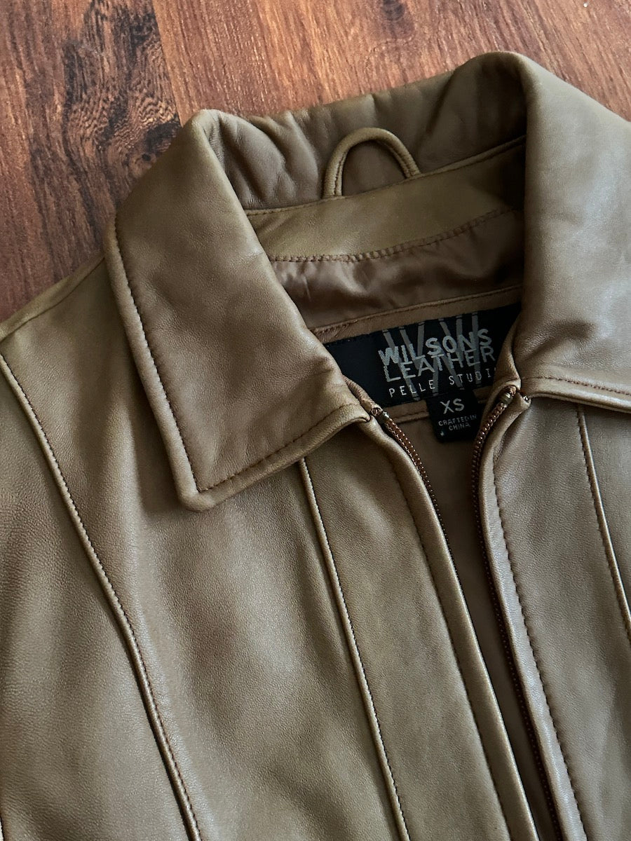 Brown leather jacket with a Wilsons Leather Pelle Studio brand label on a wooden surface