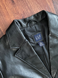 Black leather jacket with a Gap label on a wooden surface