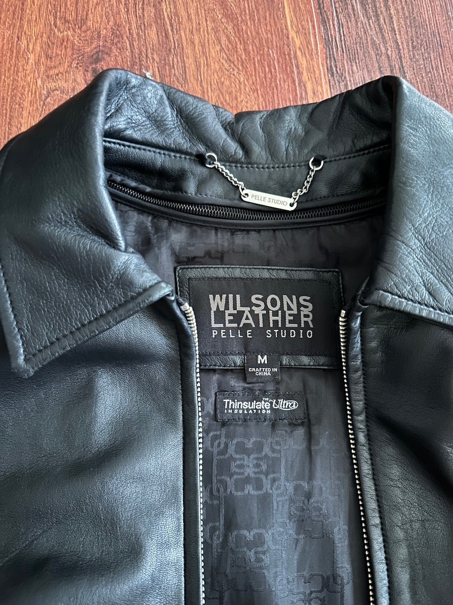 Black leather jacket with Wilsons Leather label on a wooden surface