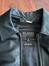 Black leather jacket with Wilsons Leather label on a wooden surface