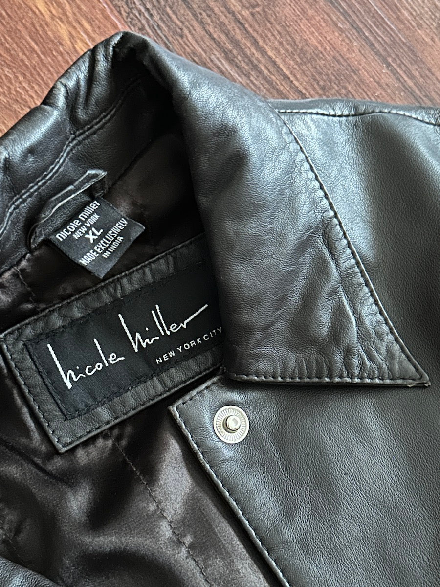Chocolate brown leather jacket with 'Nicole Miller' label on a wooden surface