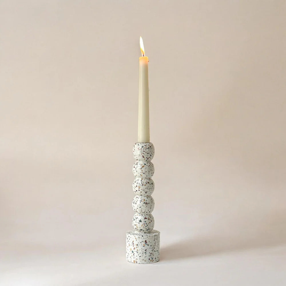 Speckled terrazzo candle holder with a lit candle on a plain background