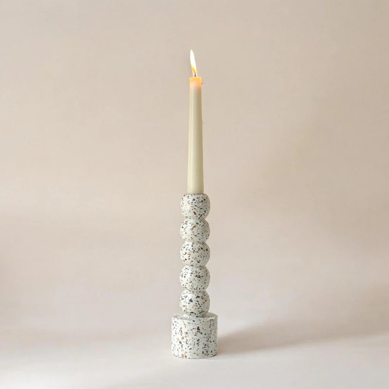 Speckled terrazzo candle holder with a lit candle on a plain background