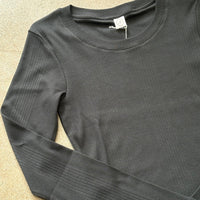 Black ribbed cotton long-sleeve shirt on a beige surface