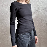Person wearing a black long-sleeve top and jeans against a neutral wall.