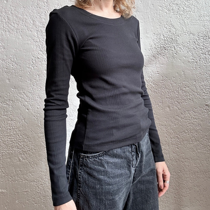 Person wearing a black long-sleeve top and jeans against a neutral wall.