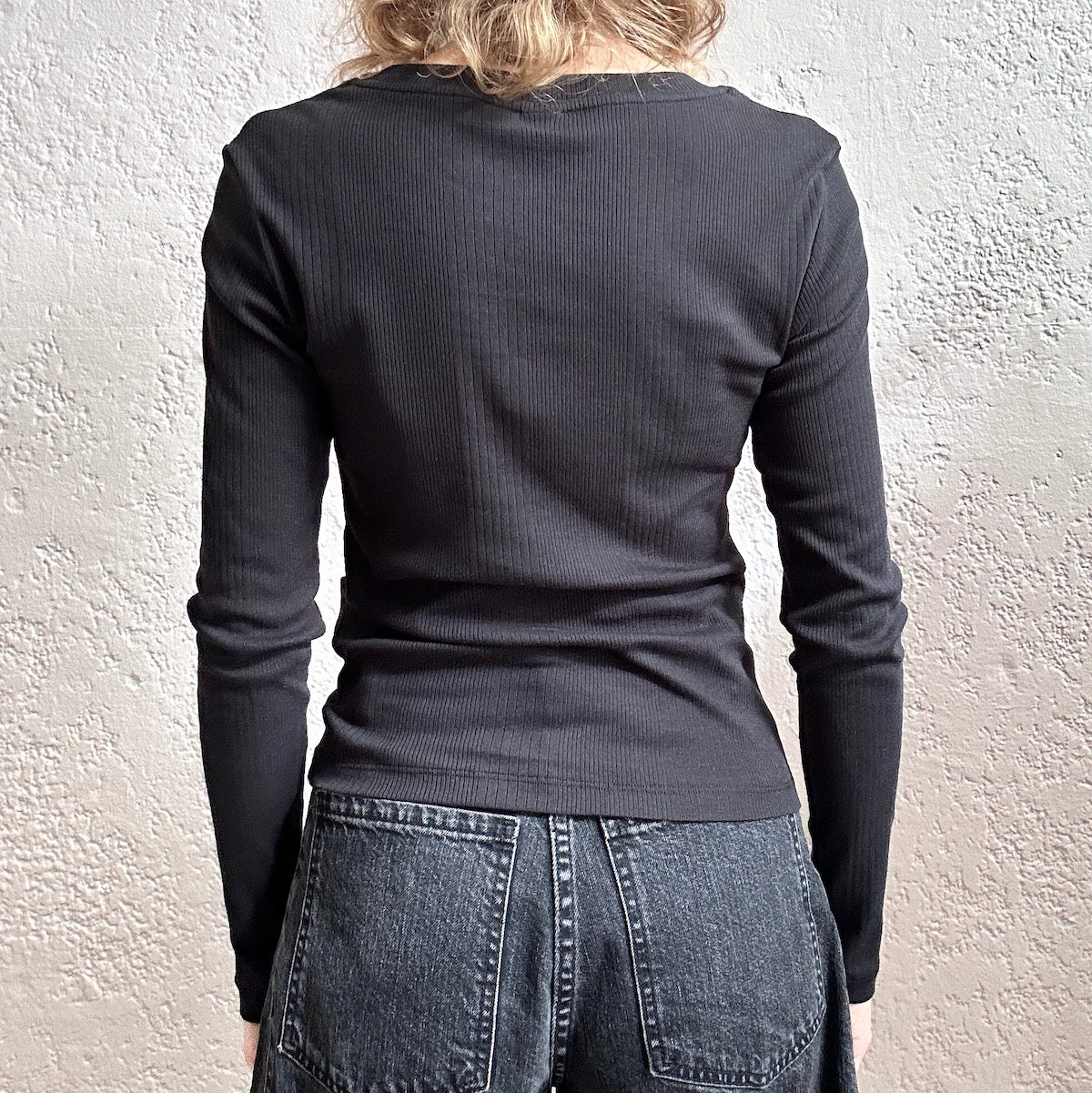Person wearing a black ribbed top and jeans against a light textured wall