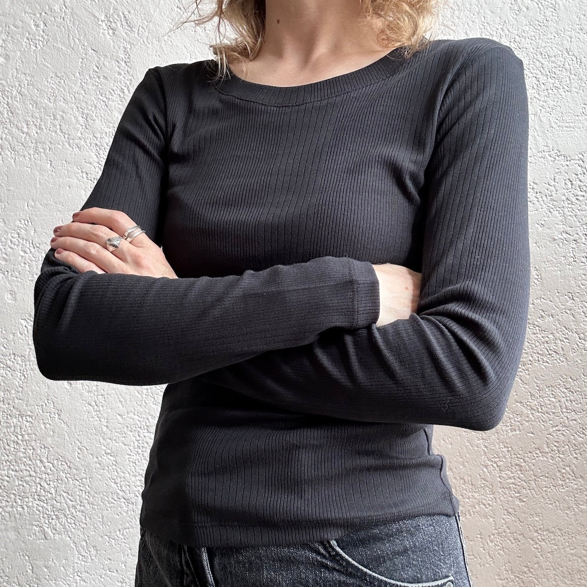 Person with arms crossed wearing a black ribbed top against a light background
