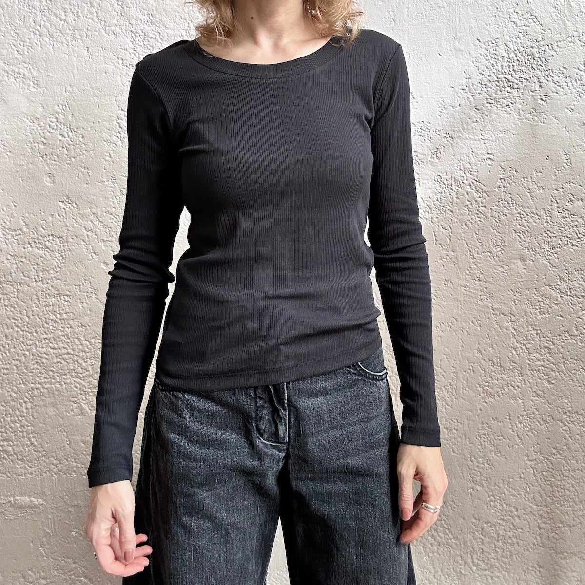 Person wearing a black long-sleeve shirt and dark jeans against a plain background