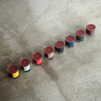 row of candles in glass jars with colorful labels on a cement surface