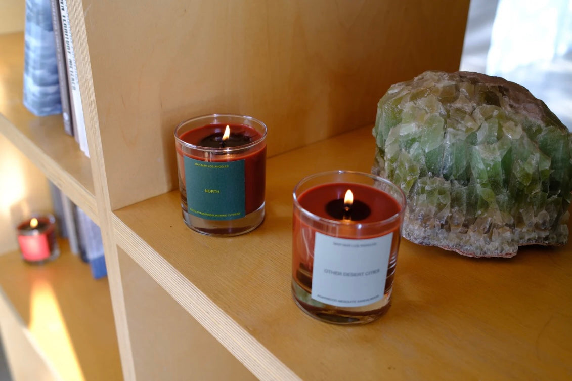 Two lit candles on a wooden shelf with a large crystal rock.