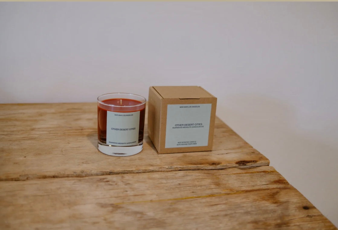 Candle and its packaging on a wooden surface with a plain background