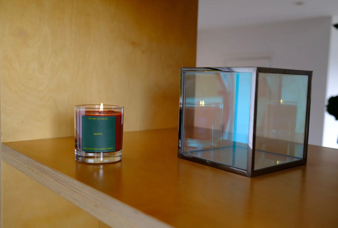Candle in a glass vessel on a wooden surface with a glass box nearby