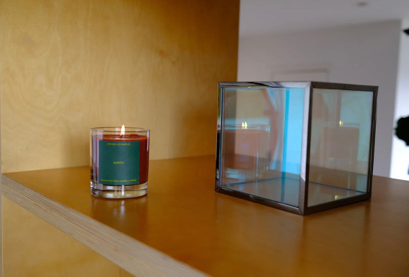Candle in a glass vessel on a wooden surface with a glass box nearby