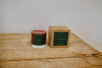Candle in a glass vessel next to its cardboard box on a wooden surface