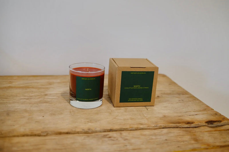Candle in a glass vessel next to its cardboard box on a wooden surface