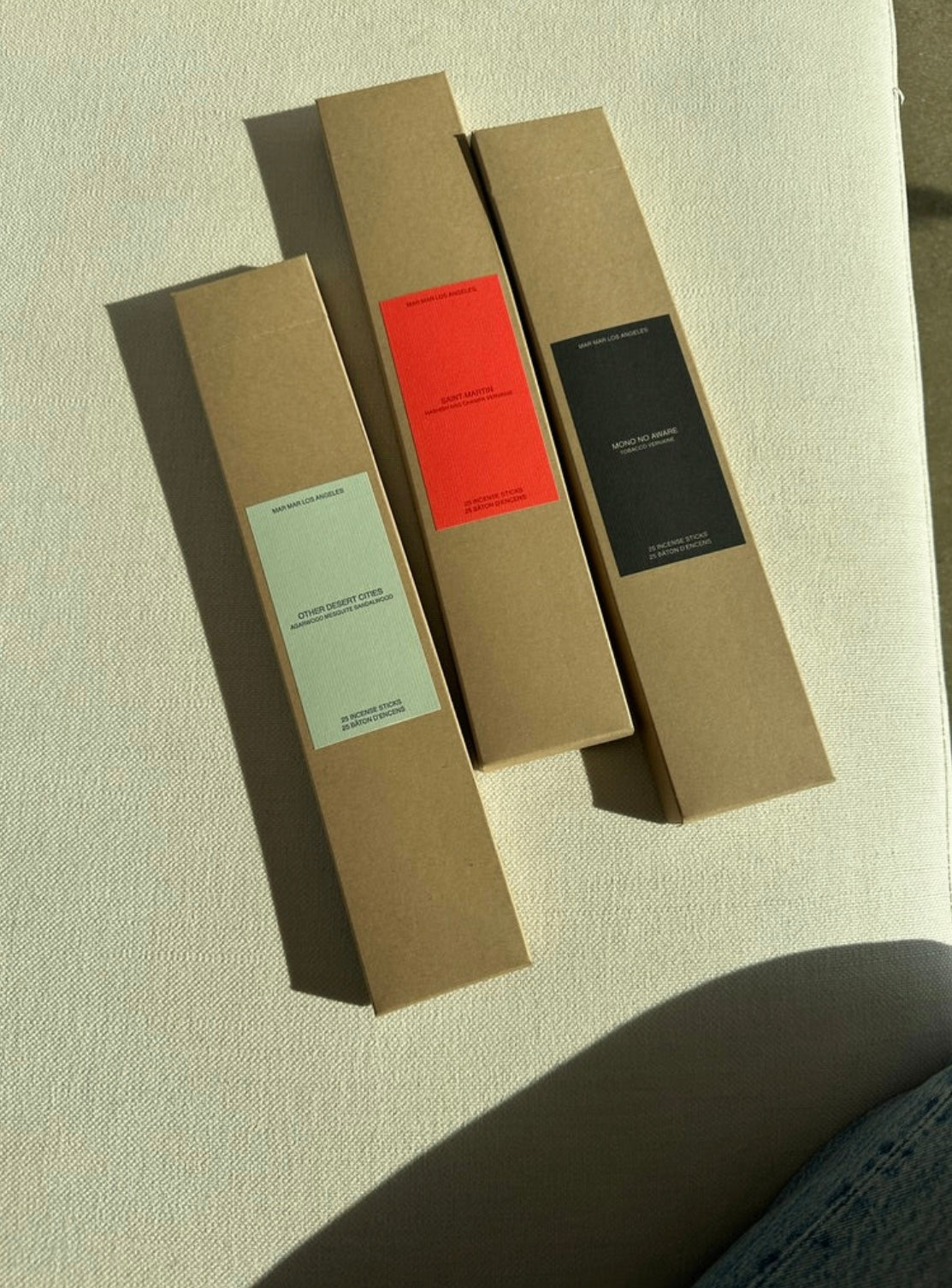 Three cardboard boxes of incense sticks with different colored labels on a textured surface