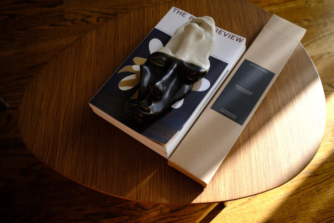 Book with a black and white mask sculpture on top next to a cardboard box of incense on a wooden surface