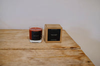 Candle and its packaging on a wooden surface with a plain background