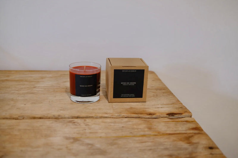 Candle and its packaging on a wooden surface with a plain background