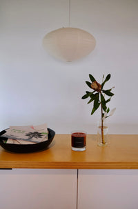 Small table with a glass jar candle, a bowl with books, and a plant against a white wall.