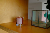 Candle with a label on a wooden surface next to a glass container
