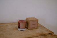 Candle in a glass jar next to a cardboard box on a wooden surface with a white background
