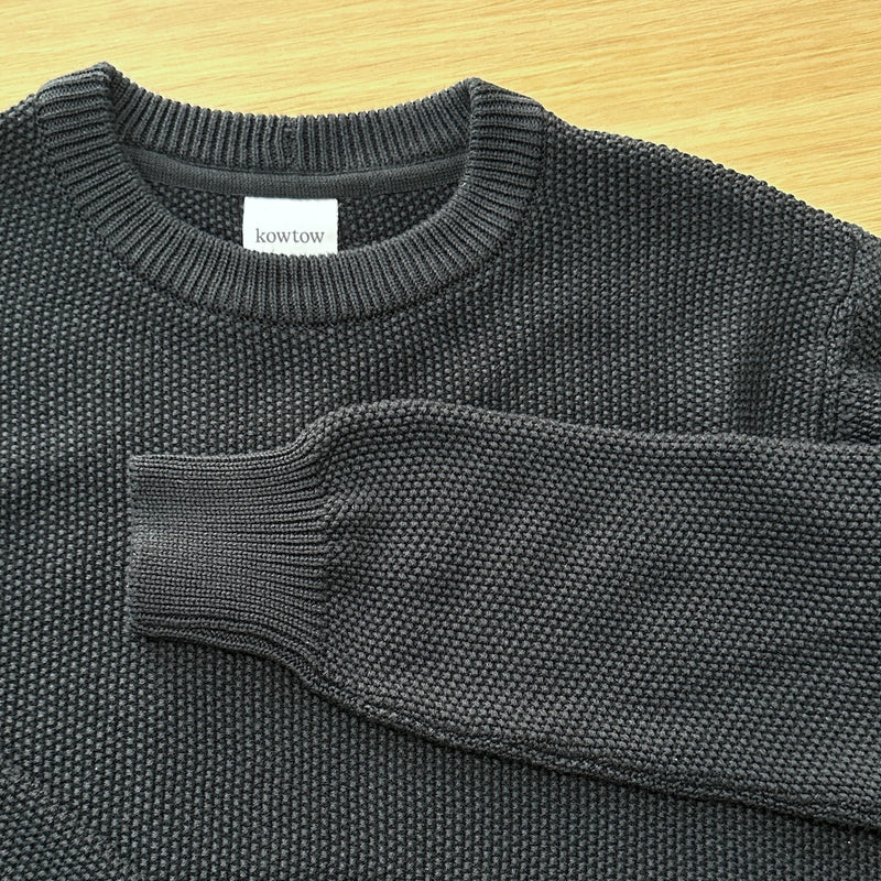 Black knit sweater with 'kowtow' label on a wooden surface