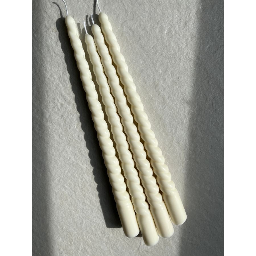 Four white ribbed spiral taper candles on a light gray background